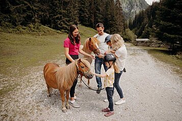 Die Familie die mit einem Pony spazieren gehen umgeben mit Bergen und Bäumen.
