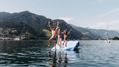 Kinder springen gemeinsam von einer Badeplattform in den Zeller See direkt beim Familienhotel Amiamo, mit Bergpanorama im Hintergrund.