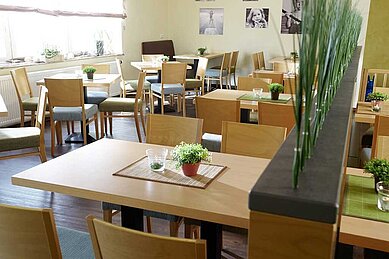 Einladendes Restaurant im Familienhotel Deichkrone mit hellen Holztischen und Stühlen, dekoriert mit frischen Pflanzen, um ein gemütliches Ambiente für die Essenszeit der Gäste zu schaffen.