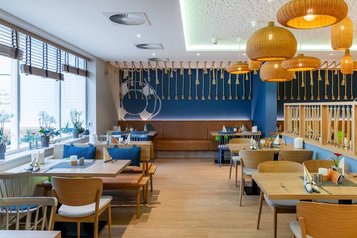 Einladendes Restaurant im Familienhotel Deichkrone mit hellen Holztischen und Stühlen, dekoriert mit frischen Pflanzen, um ein gemütliches Ambiente für die Essenszeit der Gäste zu schaffen.
