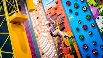 Kind mit Helm und Klettergurt an einer bunten Indoor-Kletterwand in einer Kletterhalle.