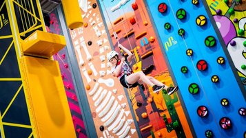 Kind mit Helm und Klettergurt an einer bunten Indoor-Kletterwand in einer Kletterhalle.