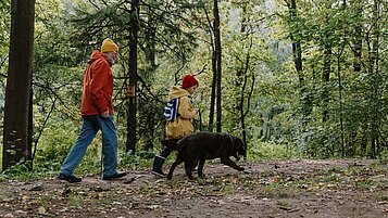 Opa und Enkel wandern mit Hund im Urlaub im Bayerischen Wald.