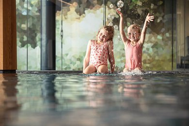 Zwei Mädchen plantschen lachend im Innenpool eines Familienhotels