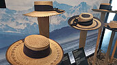 Ein besonders interessanter Ausflug ist die Hut Ausstellung im Allgäu. Hier werden Hüte auf einem Balken vor einem Bergpanorama präsentiert.