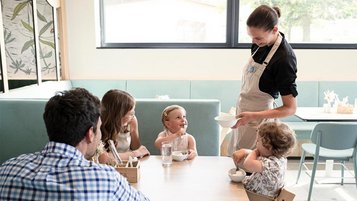 Eine Servicekraft serviert Eis an den Familientisch im Restaurant des Familienhotels.