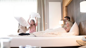 Vierköpfige Familie tobt im Bett und macht eine Kissenschlacht