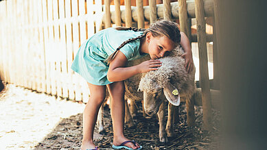 Ein Mädchen streichelt im Freilaufgehege ein Schaf im Familienhotel Post Family Resort im Salzburger Land.