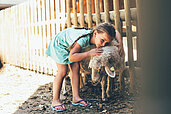 Ein Mädchen streichelt im Freilaufgehege ein Schaf im Familienhotel Post Family Resort im Salzburger Land.