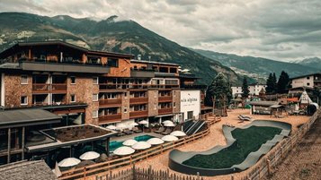 Außenansicht des Familienhotel Mia Alpina in Tirol mit Pool, Liegen, Sonnenschirmen und Bergen im Hintergrund.