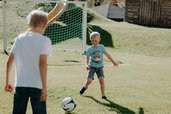 Zwei Kinder spielen auf einer Wiese vor einem Tor Fußball im Außenbereich des Familienhotels Oberkarteis.