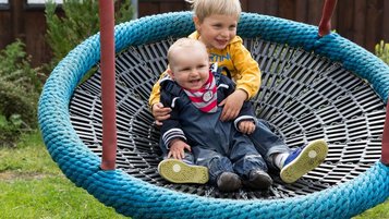 Zwei Kinder sitzen in einer Nestschaukel im Aussenbereich des Familienhotels Alphotel
