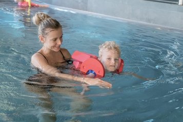 Eine Frau unterstützt ein Kind mit Schwimmhilfe beim Schwimmen im Hallenbad des Familienhotels Gorfion in Liechtenstein.