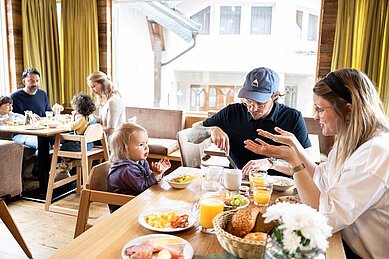 Dreiköpfige Familie mit Kleinkind sitzt am gedeckten Frühstückstisch im Familienhotel Sonnenpark.