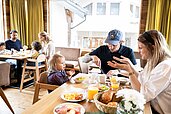 Dreiköpfige Familie mit Kleinkind sitzt am gedeckten Frühstückstisch im Familienhotel Sonnenpark.