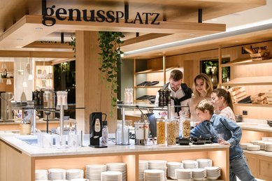 Familie wählt am Frühstücksbuffet des Zauchenseehofs aus verschiedenen Cerealien und Zutaten aus und genießt die moderne, helle Buffetstation.