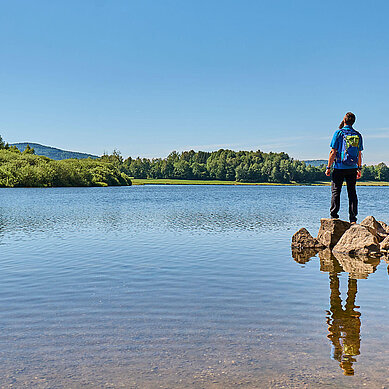 Drei Wandere stehen am Perlsee im Bayerischen Wald und genießen die Sonne.