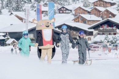 Kinder im Winter mit einem Maskottchen vor dem Familienhotel Gorfion in Liechtenstein.