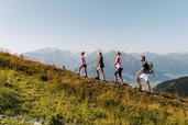 Eine Familie wandert sportlich über einen Berghang mit weitem Alpenblick – Naturerlebnis direkt vom Familienhotel Amiamo aus.