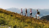 Eine Familie wandert sportlich über einen Berghang mit weitem Alpenblick – Naturerlebnis direkt vom Familienhotel Amiamo aus.