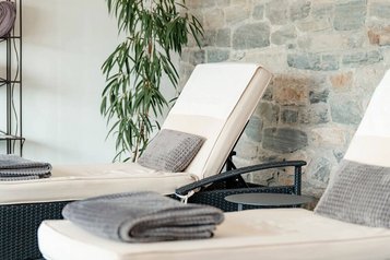 Zwei gepolsterte Liegen mit grauen Handtüchern vor einer Steinwand, daneben eine grüne Pflanze im Wellnessbereich des Familienhotels Amiamo.