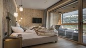Gemütliches Schlafzimmer im Familienhotel Mia Alpina in Tirol mit großem Bett, Terrasse und Blick auf die Berge.