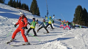 Kind mit Helm und Skiausrüstung steht auf verschneiter Piste vor einer malerischen Bergkulisse, was Wintersportaktivitäten für Kinder in einem familienfreundlichen Hotelumfeld veranschaulicht.