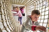 Zwei Kinder klettern im Indoor-Spielplatz in einem Netz im Familienhotel Amiamo im Salzburger Land