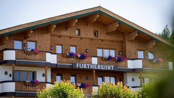 Außenansicht des Familienhotels Landgut Furtherwirt mit blumengeschmückten Balkonen und traditioneller Holzfassade.