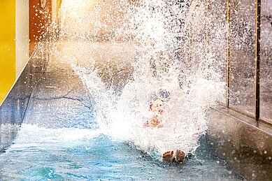 Kind rutscht auf der Wasserrutsche im Familienhotel Sonnenpark in ein Wasserbecken.