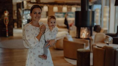 Eine Mutter steht mit Kind im Arm in der Lounge des Familienhotel Mia Alpina in Tirol.