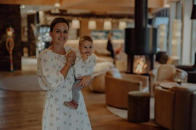 Eine Mutter steht mit Kind im Arm in der Lounge des Familienhotel Mia Alpina in Tirol.