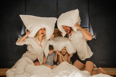Familie tollt lachend im Bett eines Zimmers im Zauchenseehof herum und hält sich spielerisch große Kissen über den Kopf.