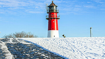 Der Leuchtturm in Büsum an der Nordsee strahlt im Sonnenschein im Winter.