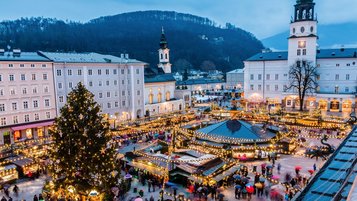 Ein festlich geschmückter Weihnachtsmarkt in Salzburg erstrahlt in warmem Lichterglanz, während Besucher durch die stimmungsvollen Gassen schlendern und die weihnachtliche Atmosphäre genießen