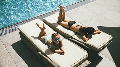 Mama und Tochter liegen am Pool auf den Liegen und sonnen sich im Familienhotel Post Family Resort im Salzburger Land.