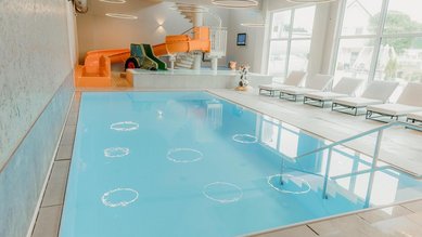 Helles Hallenbad im Familienhotel Friedrichshof in Bayern mit Pool, Liegen und großen Fenstern.