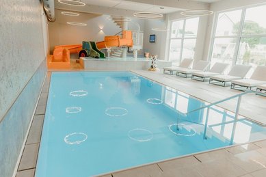 Helles Hallenbad im Familienhotel Friedrichshof in Bayern mit Pool, Liegen und großen Fenstern.