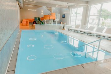 Helles Hallenbad im Familienhotel Friedrichshof in Bayern mit Pool, Liegen und großen Fenstern.