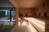 Sauna im Spa Bereich des Familienhotel Bella Vista in Südtirol mit Holzliegen, warmem Licht und Blick zum Pool.
