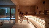 Sauna im Spa Bereich des Familienhotel Bella Vista in Südtirol mit Holzliegen, warmem Licht und Blick zum Pool.