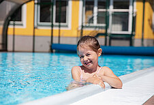 Lachendes Mädchen im Außenpool des Familienhotels Bruckwirt in Oberösterreich bei schönen Wetter im Sommer.
