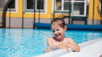 Lachendes Mädchen im Außenpool des Familienhotels Bruckwirt in Oberösterreich bei schönen Wetter im Sommer.