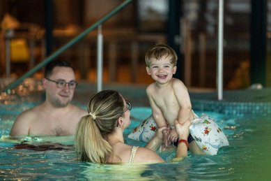 Fröhliche Familienzeit im Wasser: Im Familienhotel Elldus im Erzgebirge planschen Eltern mit ihrem Kleinkind im Pool.