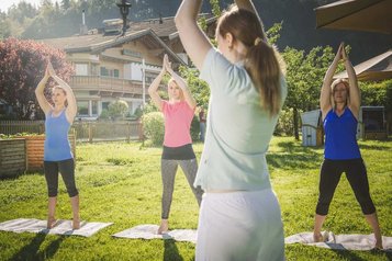 Yoga im Landgut Furtherwirt Garten, drei Frauen praktizieren Entspannungsübungen vor traumhafter Bergkulisse