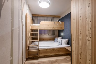 Gemütliches Familienzimmer im Zauchenseehof mit Stockbett aus Holz, großem Doppelbett und warmem, alpinem Design.