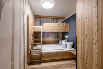 Gemütliches Familienzimmer im Zauchenseehof mit Stockbett aus Holz, großem Doppelbett und warmem, alpinem Design.