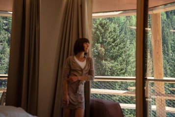 Frau steht am Balkon im Hotel Bella Vista in Südtirol und blickt in den Wald.