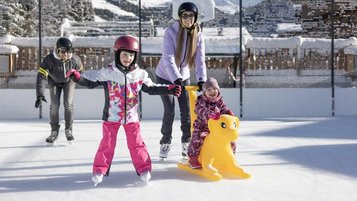 Kinder lernen das Eislaufen auf der Hoteleigenen Eislauffläche des Familienhotels Galtenberg in Tirol.