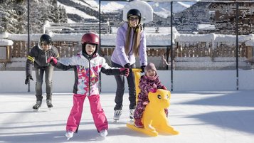 Kinder lernen das Eislaufen auf der Hoteleigenen Eislauffläche des Familienhotels Galtenberg in Tirol.